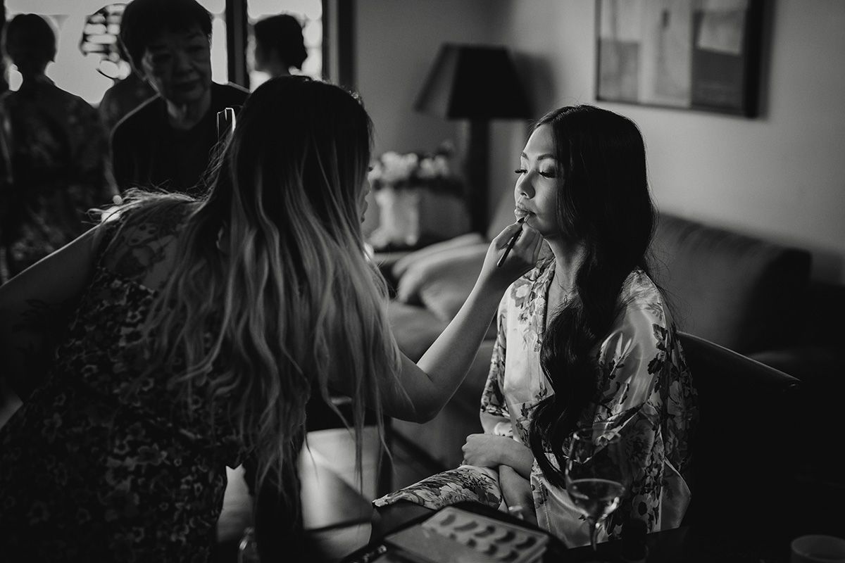 A black and white photo showing a bride having her hair and makeup applied.