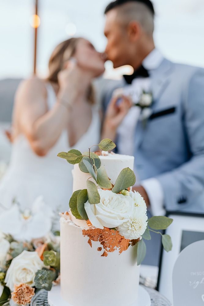 Elegant white wedding cake decorated with fresh roses and eucalyptus leaves against a soft blurred background.