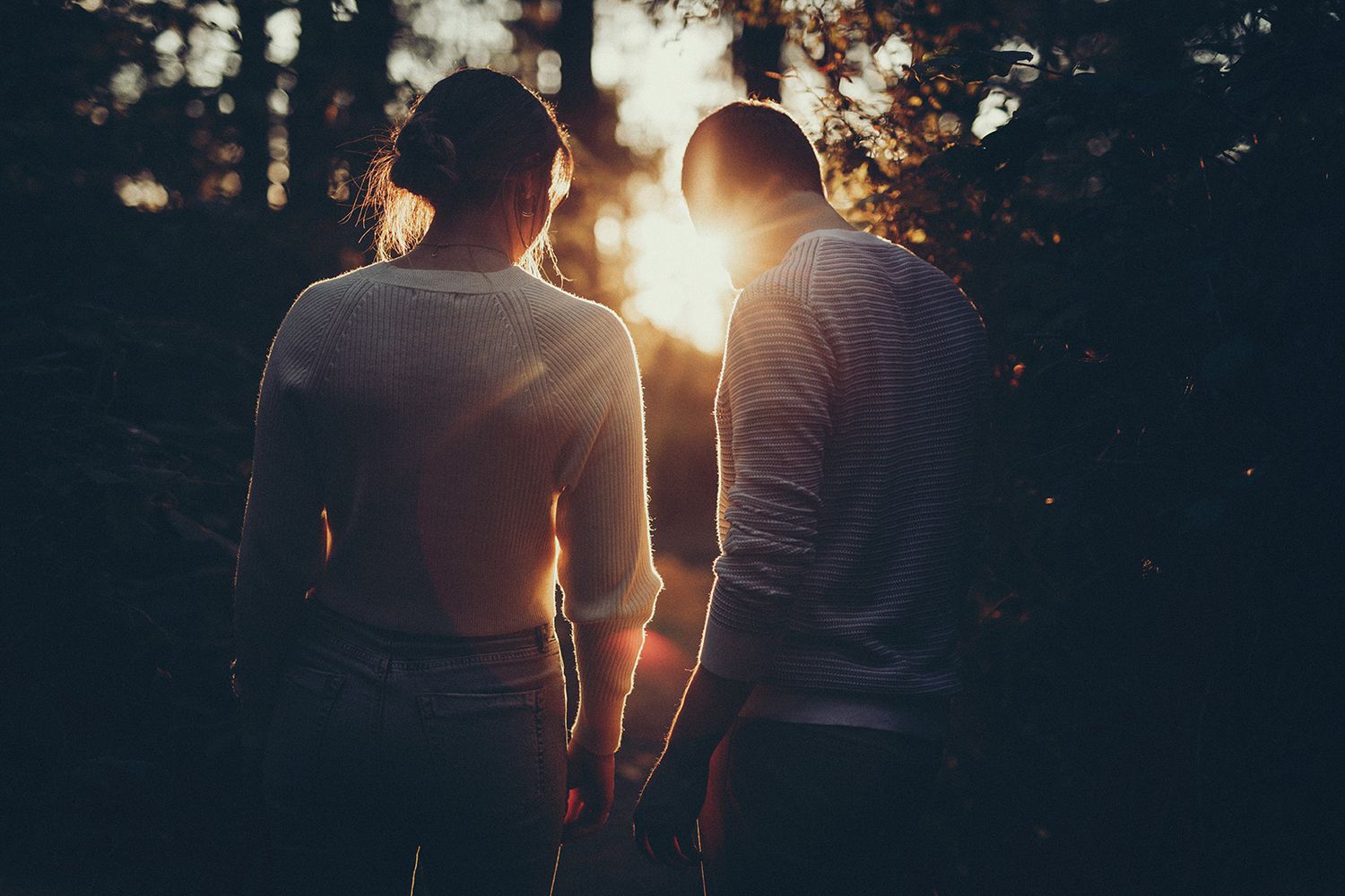 Silhouetted couple walking together at sunset with golden sunlight streaming through trees.