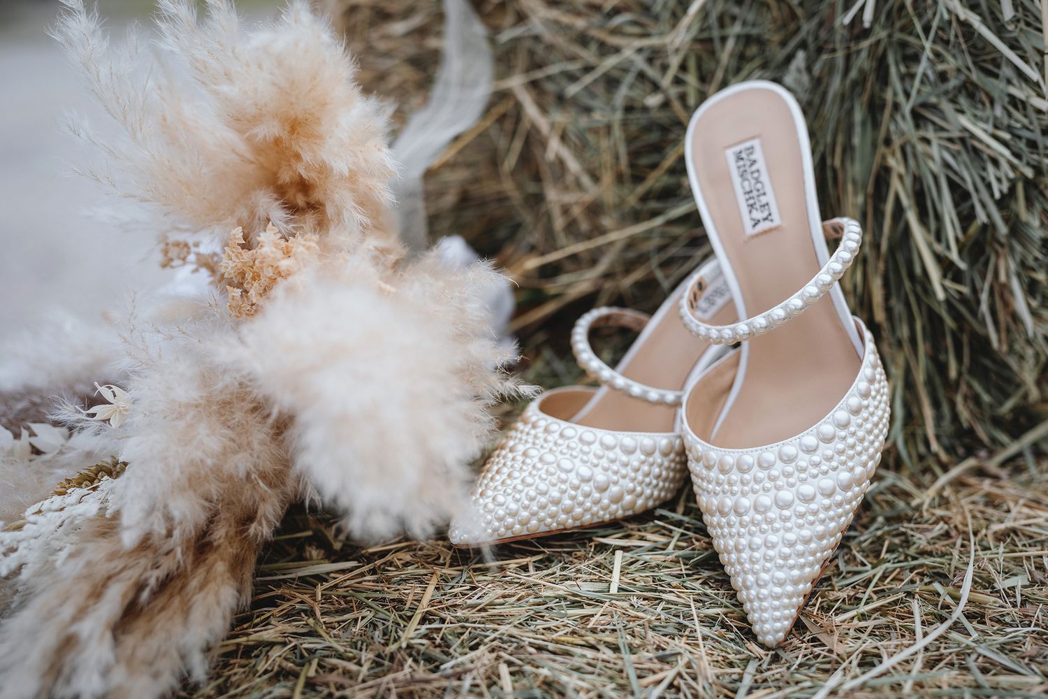 Elegant white bridal heels with pearl details arranged with dried pampas grass and neutral wedding decor elements.
