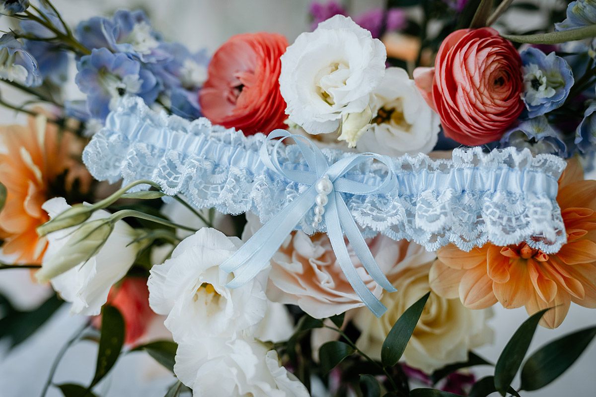 Close-up view of white and coral ranunculus flowers with delicate petals arranged in a floral design. A blue garter sits among them.