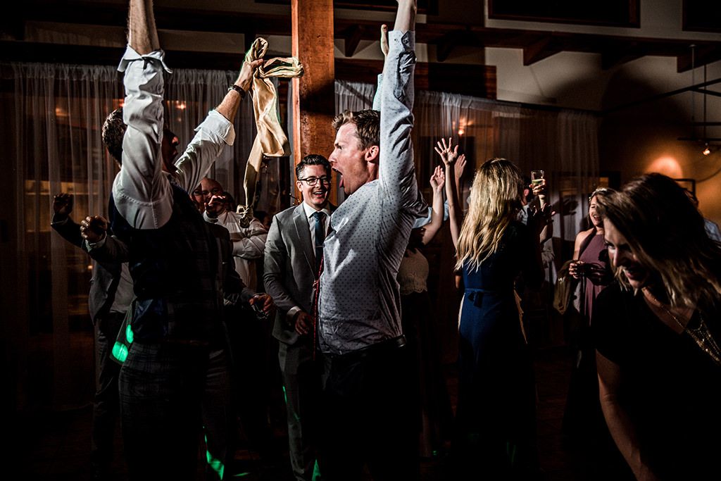 Wedding guests dance and celebrate on a dimly lit dance floor during an evening reception celebration.