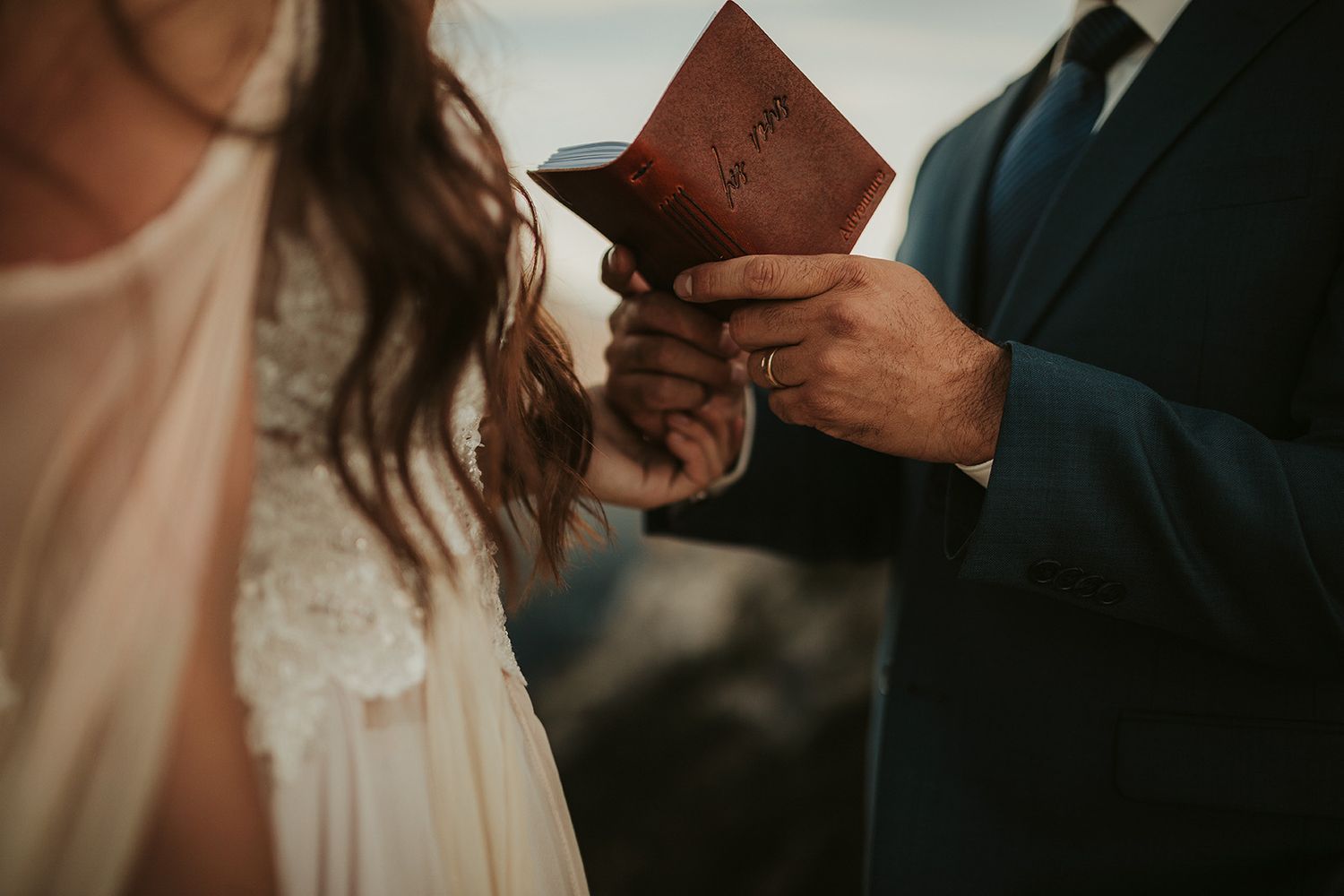 A groom holds his leather-bound vow book during an outdoor during golden hour wedding ceremony.