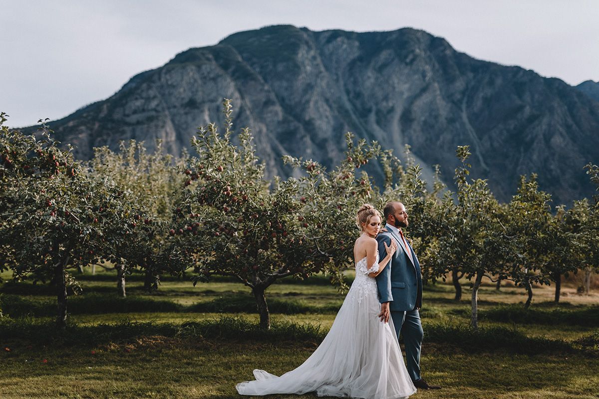 Scenic mountain wedding photos captured in an apple orchard with dramatic peaks in the background.