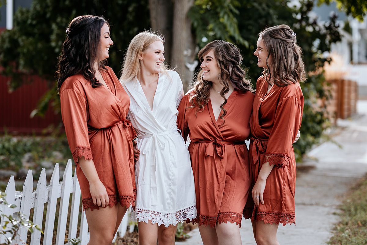 A group in coordinating rust-colored dresses and white lace outfits poses together outdoors for photos.