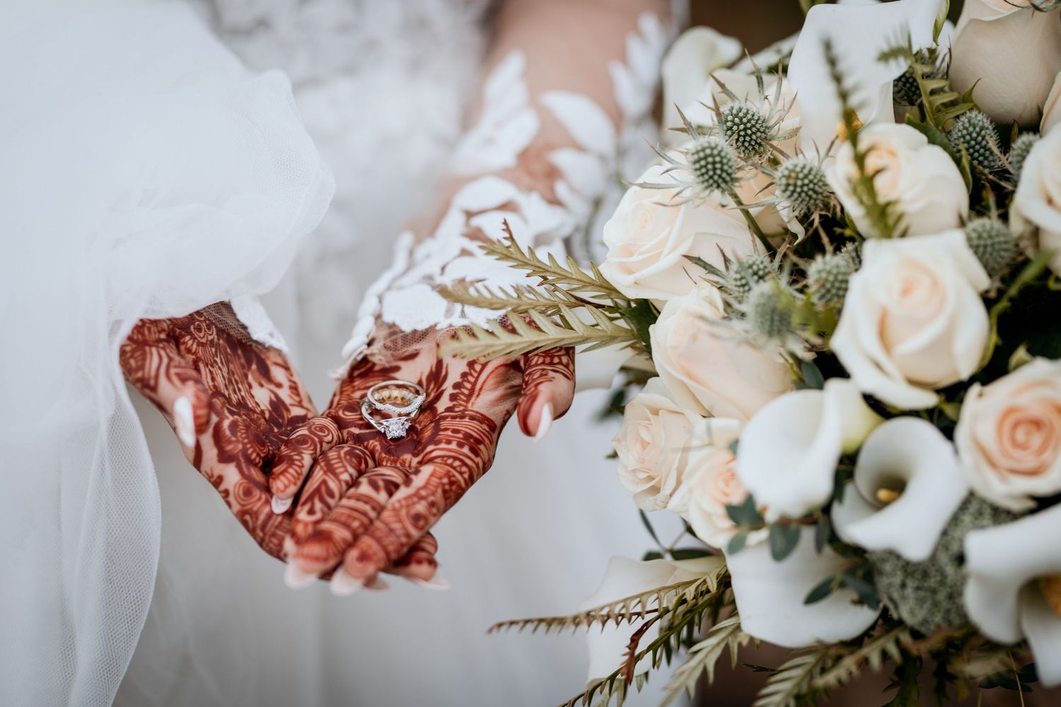A close-up of a bride's hands with traditional Mehndi tattoo. She holds the wedding rings in her palms.