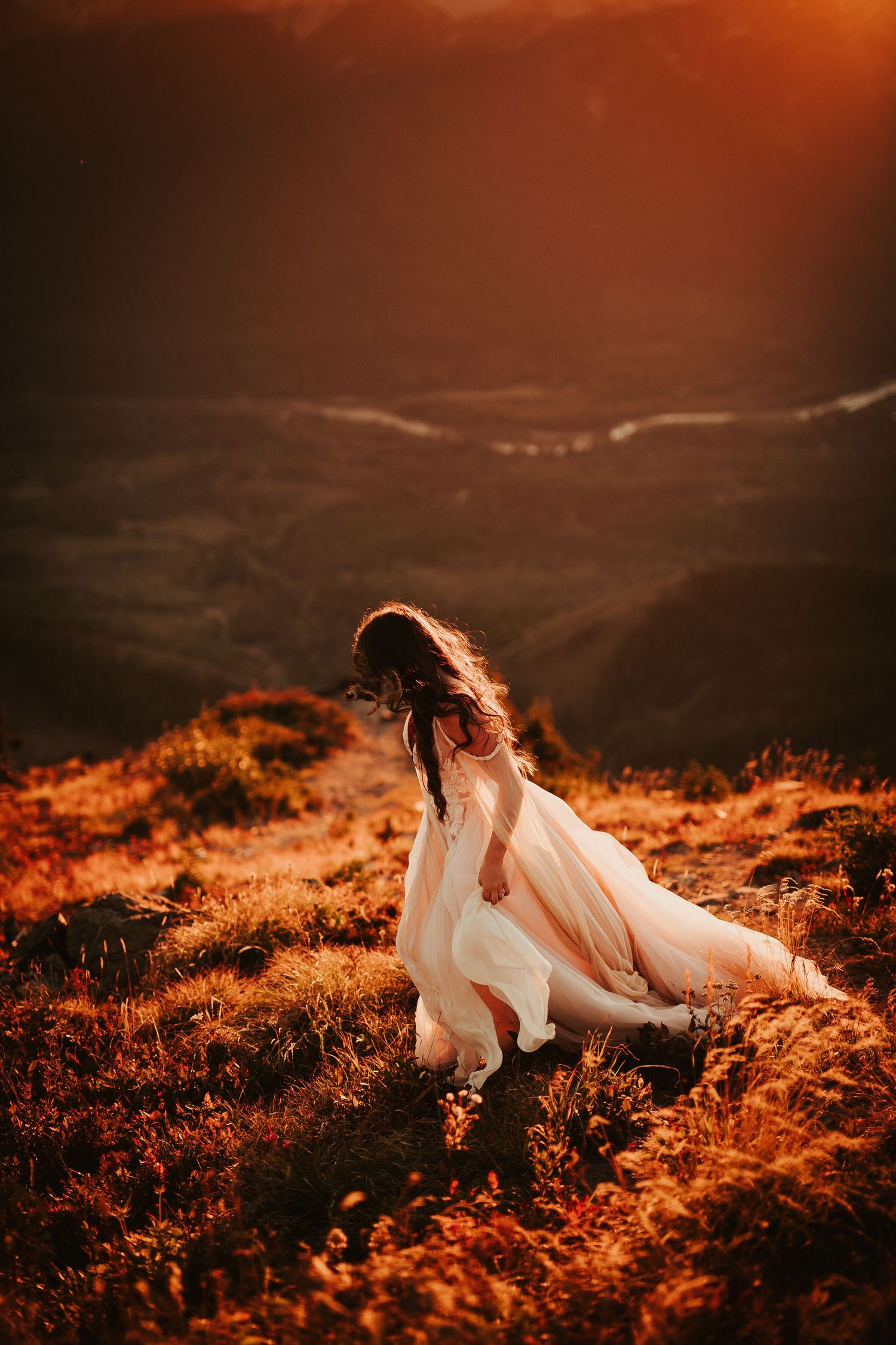 A dreamy sunset photo shoot featuring a bride in a flowing white dress lying in golden grass on a hillside.