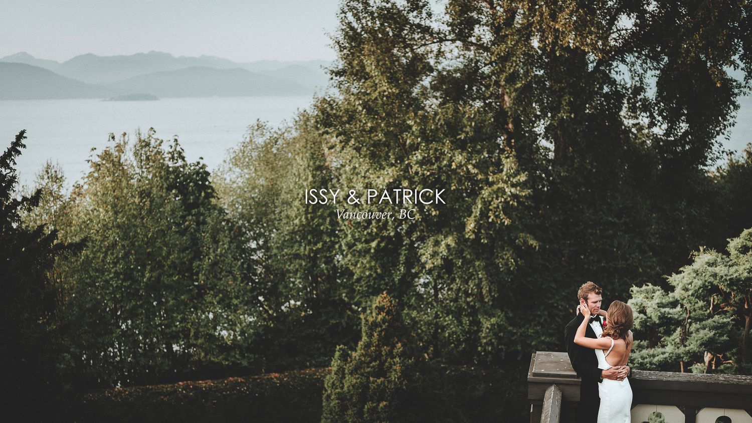 A couple embraces during a golden hour outdoor photoshoot with trees and a lake in the background.