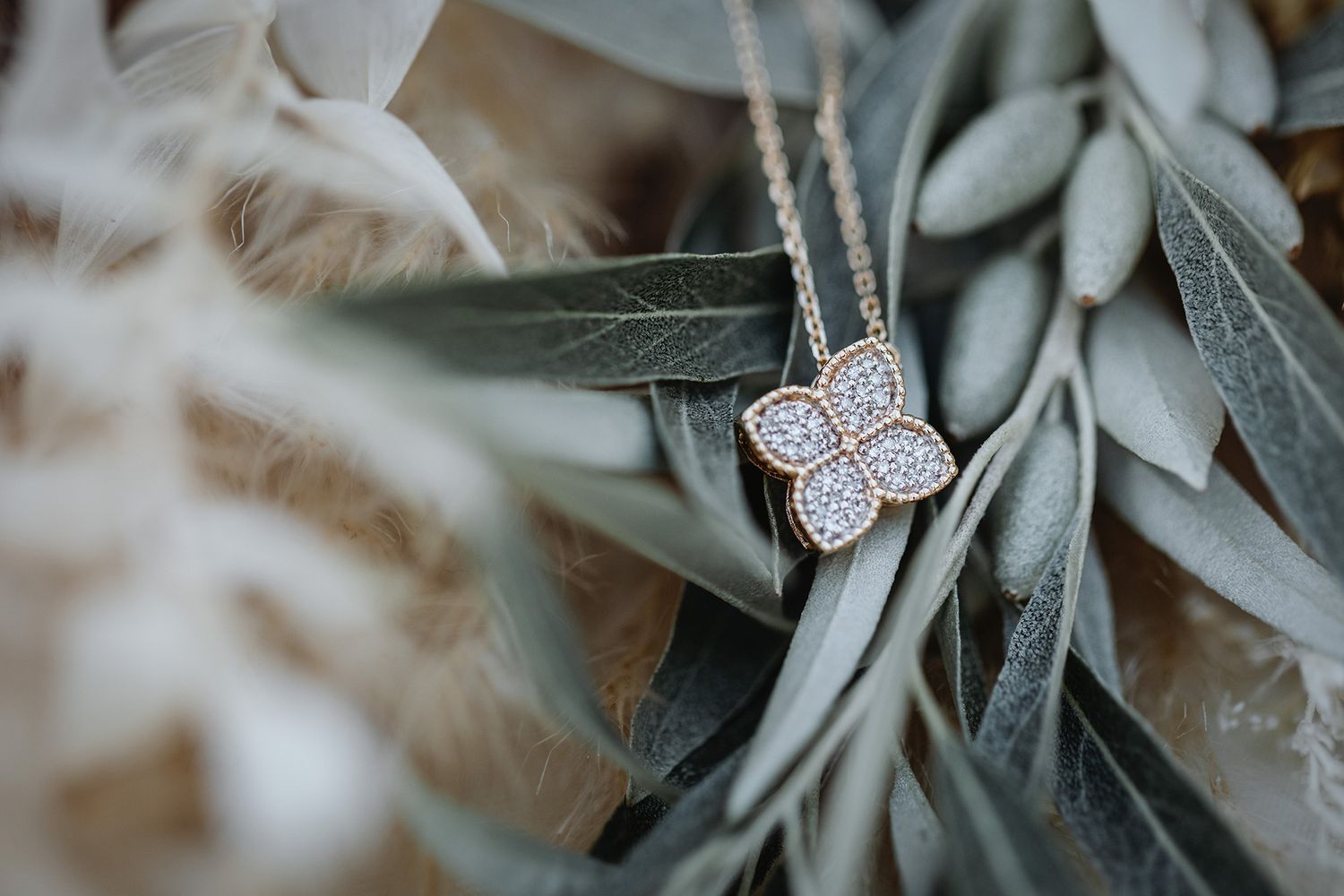 A delicate butterfly pendant necklace rests among soft green leaves in an artistic macro photograph.