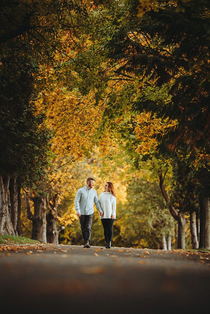 A couple walks together on a tree-lined path during autumn with golden foliage creating a romantic atmosphere.