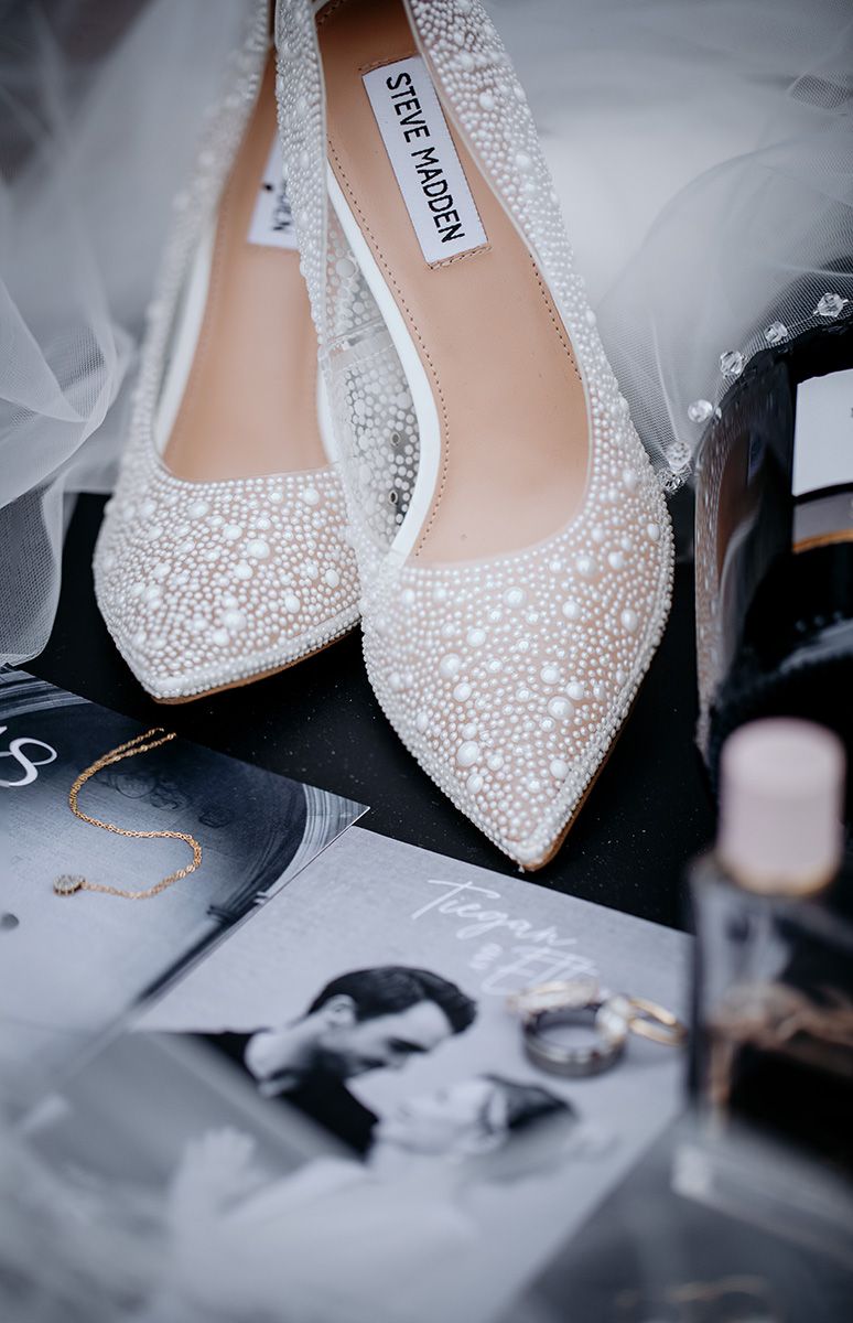 Close-up view of elegant crystal-embellished bridal shoes with delicate beading and sparkles against a dark background.