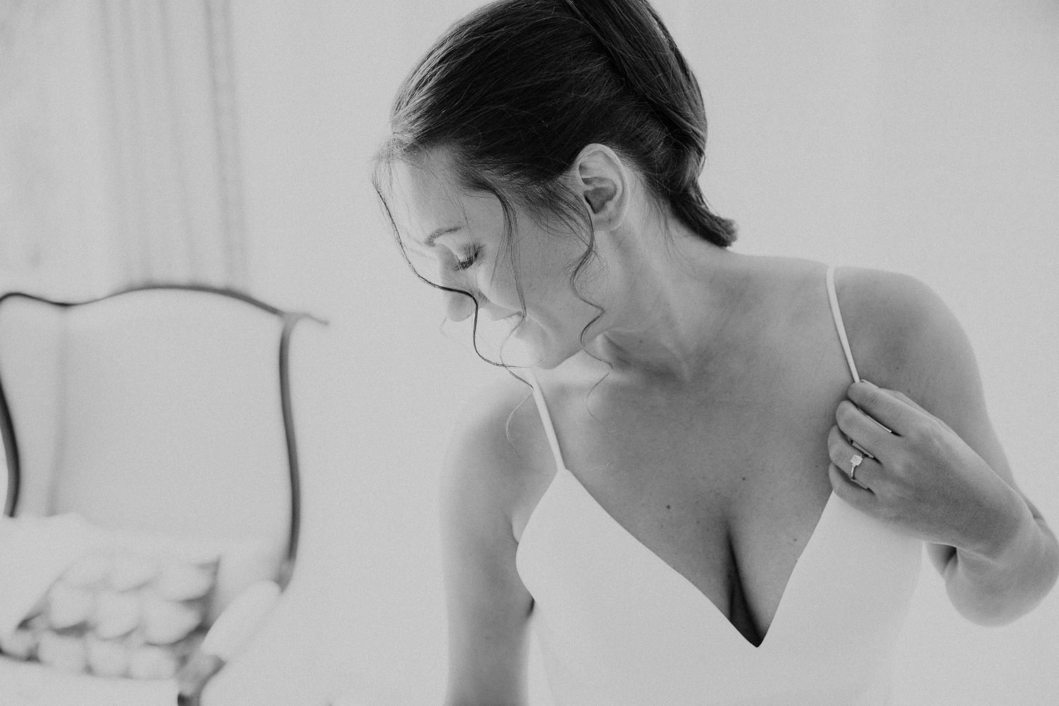 A bride getting ready for her wedding day, looking in the mirror while wearing a white dress and veil.