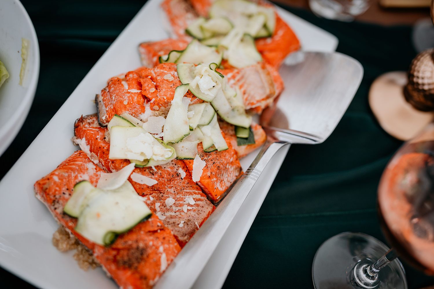 Fresh salmon topped with sliced cucumbers and herbs served on a white rectangular plate.