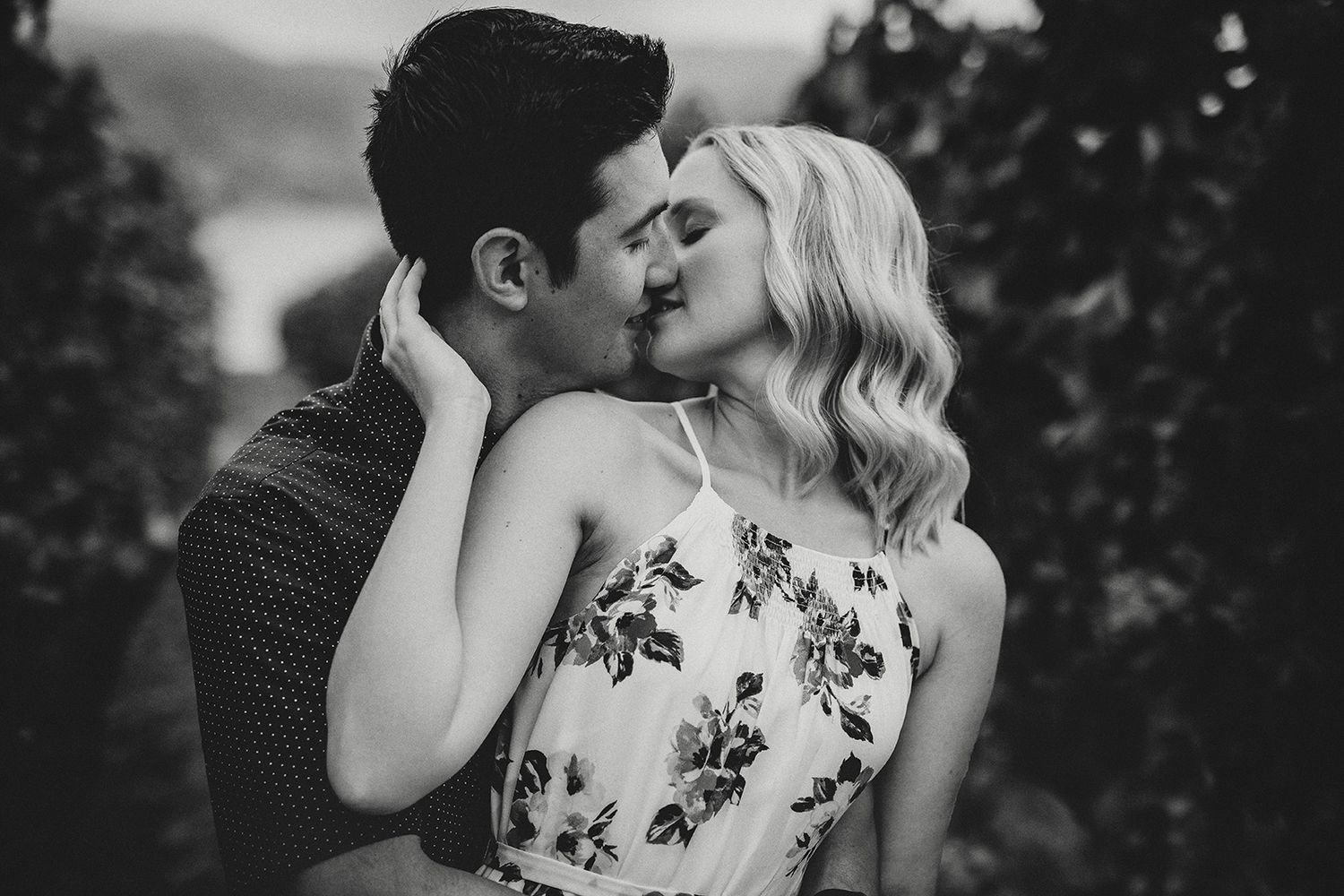 A romantic black and white photo showing a couple embracing and kissing in a vineyard..