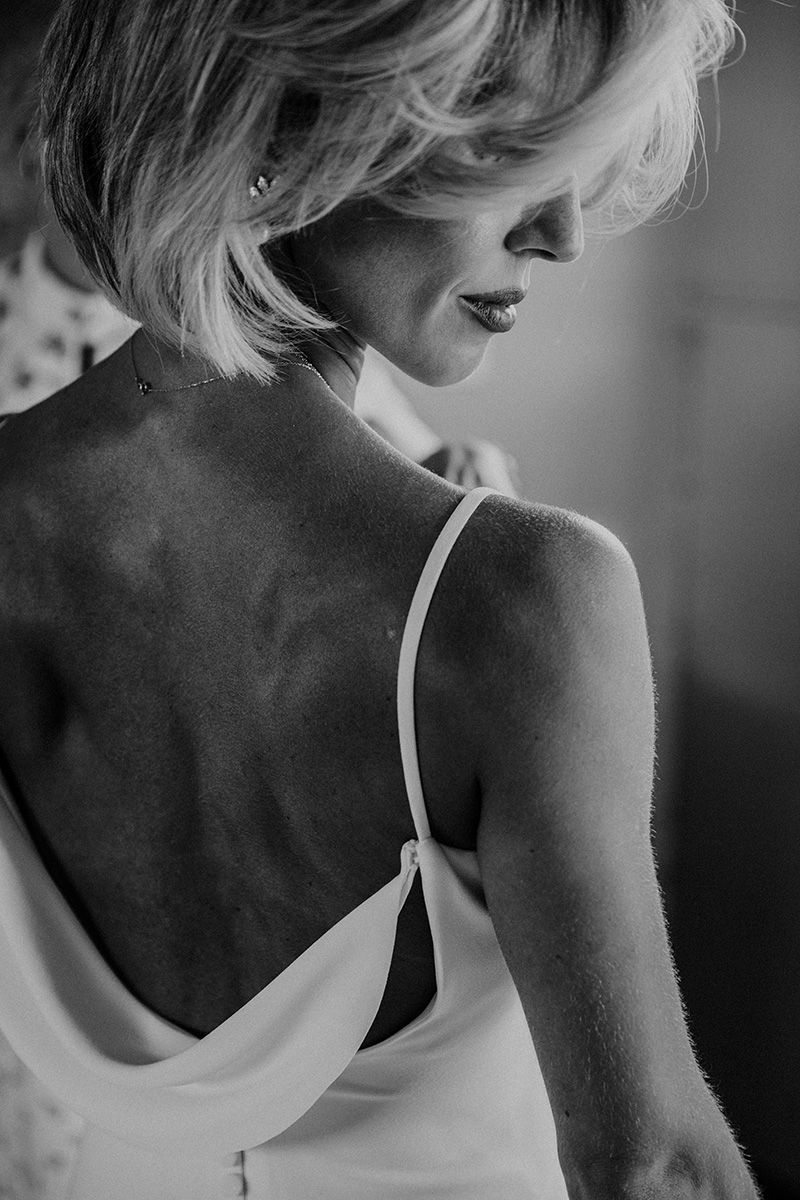 Artistic black and white photograph showing back view of a bride with blonde hair wearing white wedding dress.