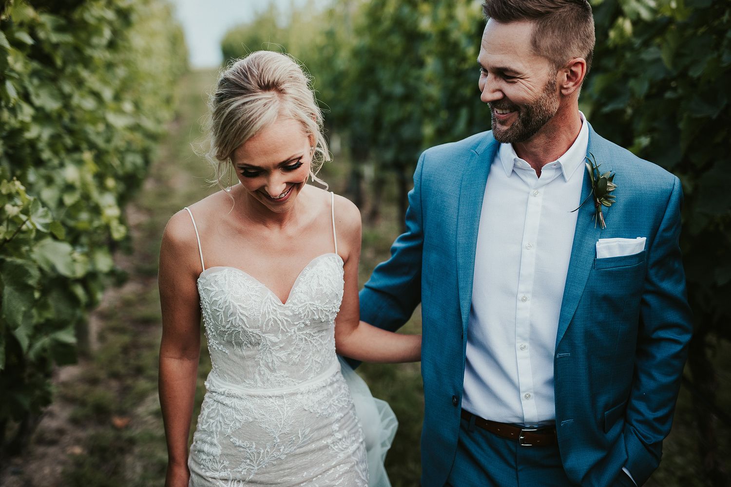 A couple in wedding attire walk together through a lush garden setting during their outdoor ceremony.