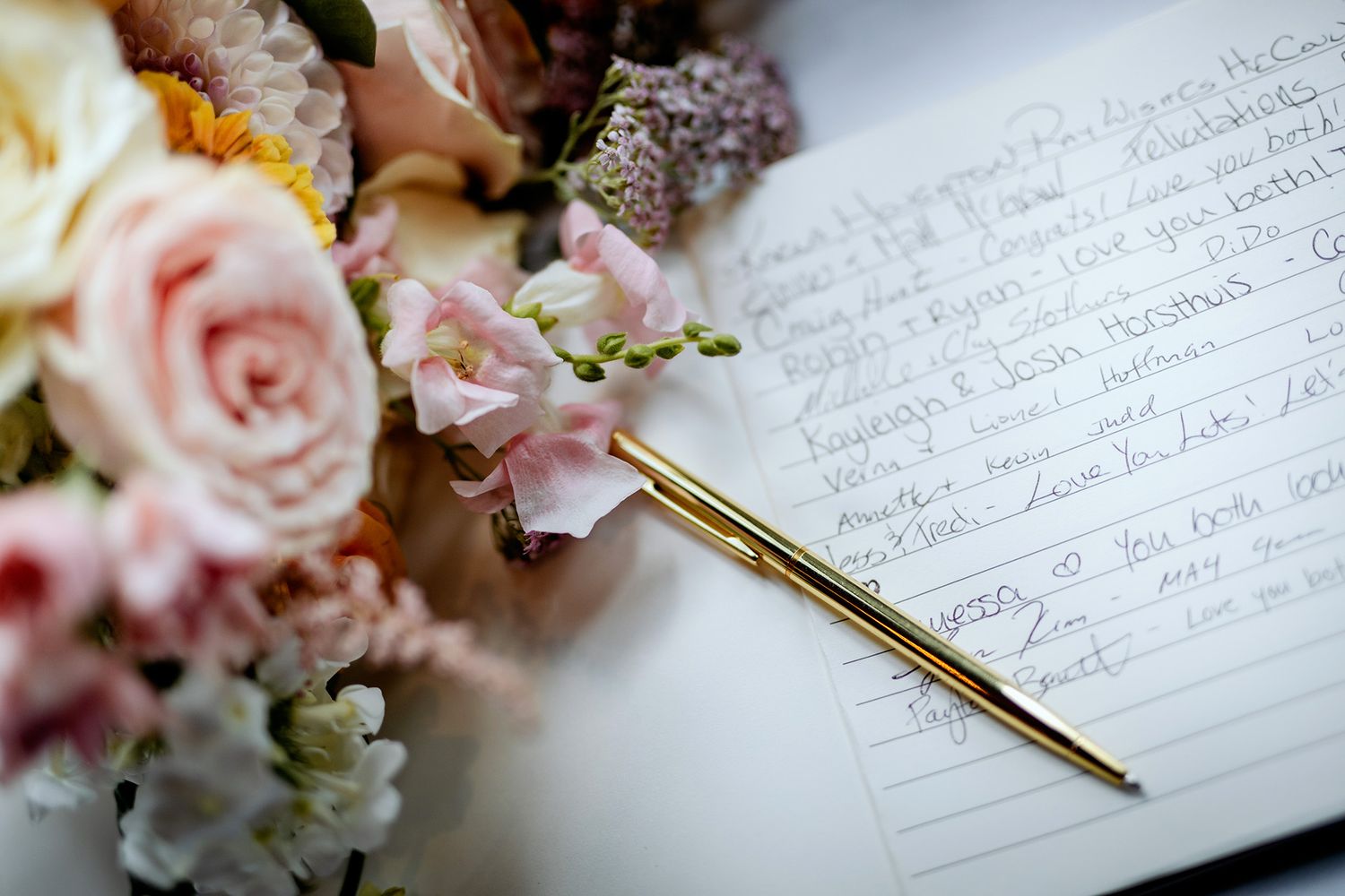 Elegant wedding details with pink roses, handwritten vows, and a gold pen on white paper.