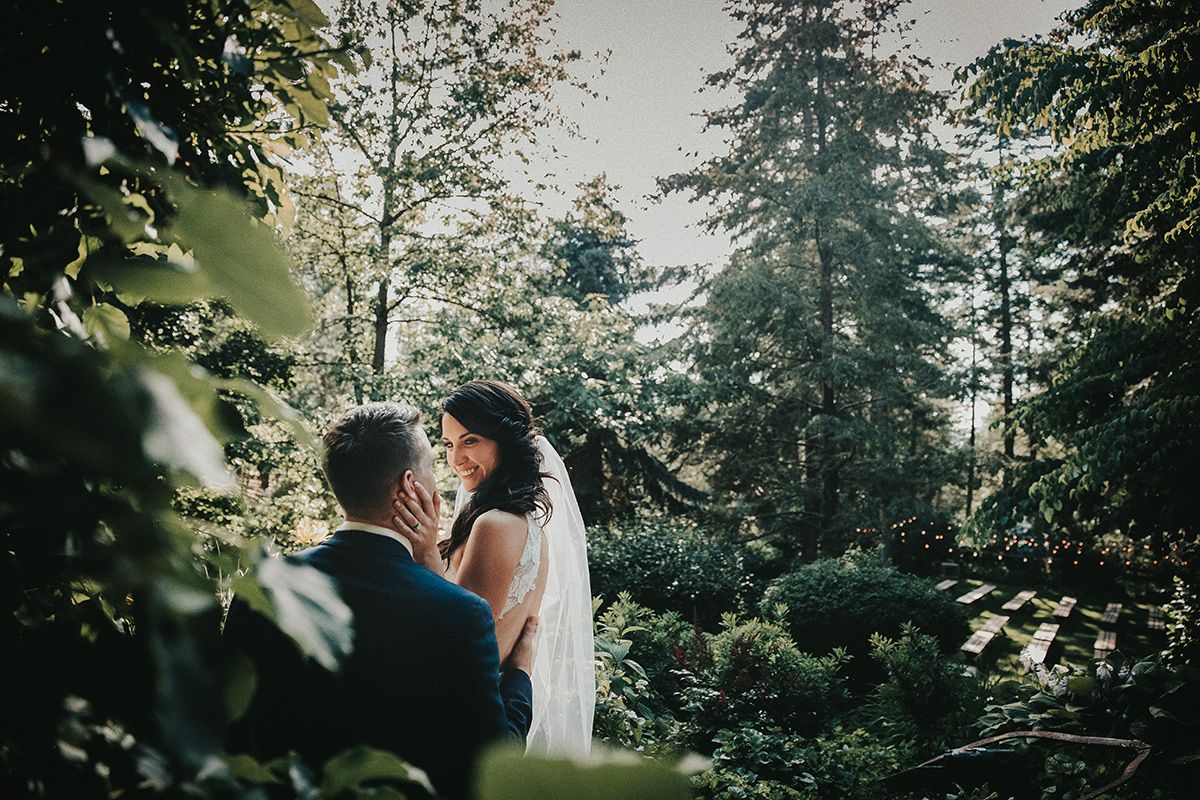 A couple shares an intimate moment surrounded by evergreen trees in a lush forest setting.