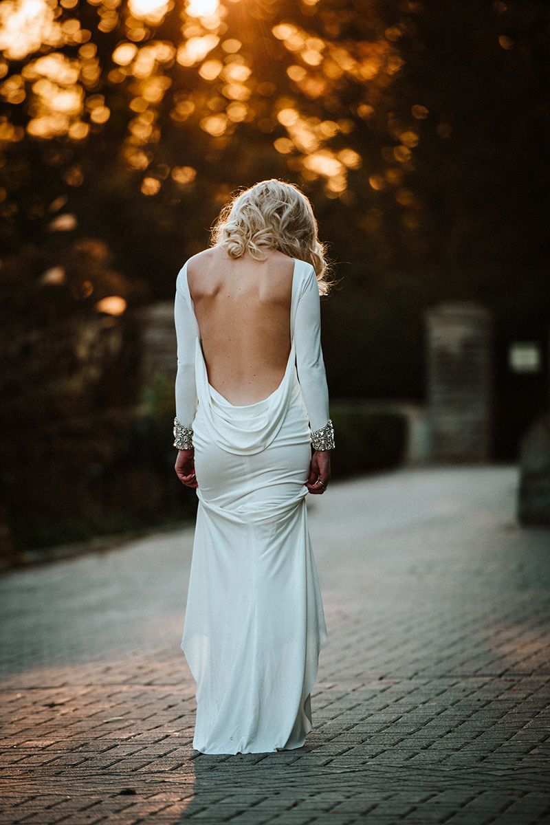 A bride in a flowing white dress walks on cobblestone during golden hour sunset creating a romantic silhouette.