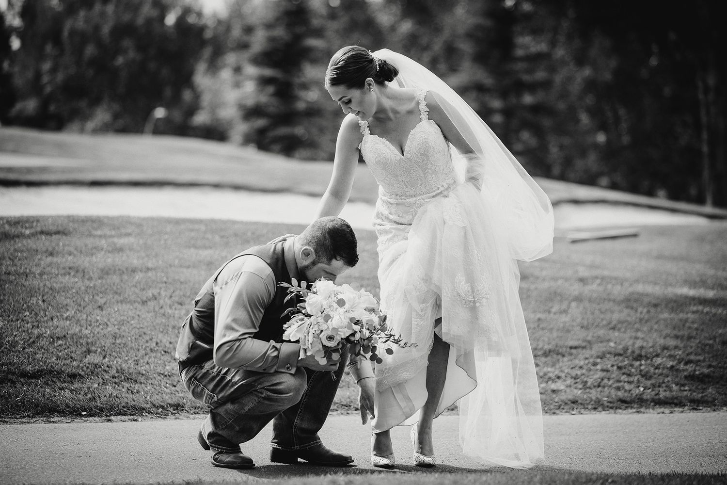 Black and white wedding photo of a groom bending down to help his bride with her shoe.