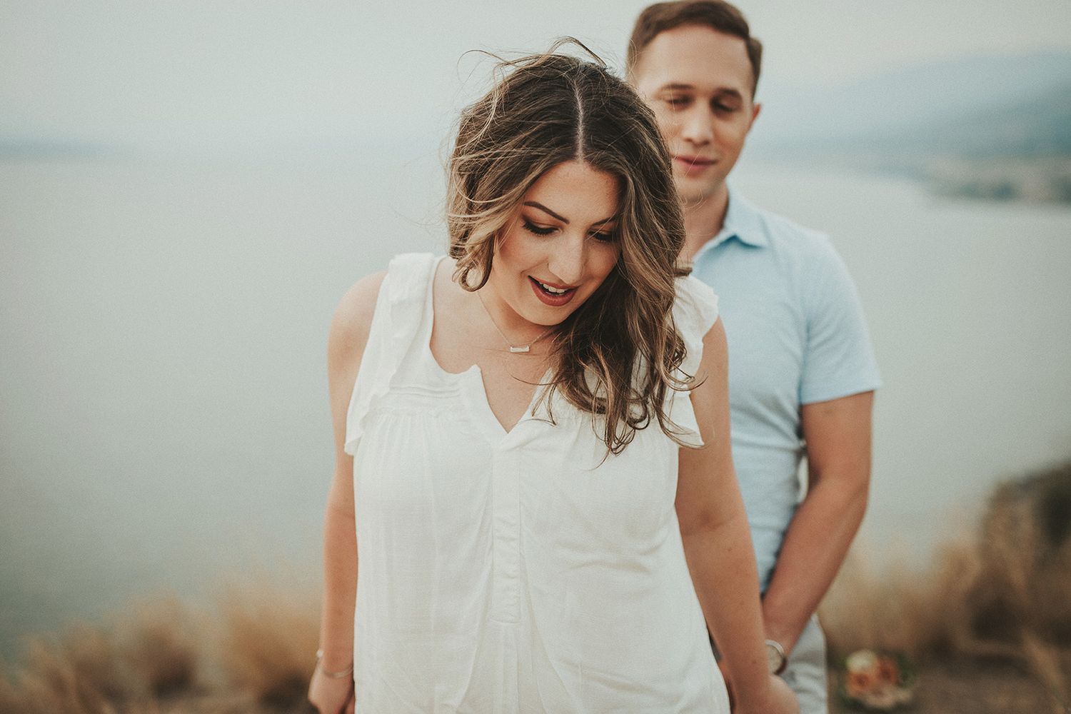 A couple walk together during an outdoor engagement photo shoot with a soft sunset backdrop.