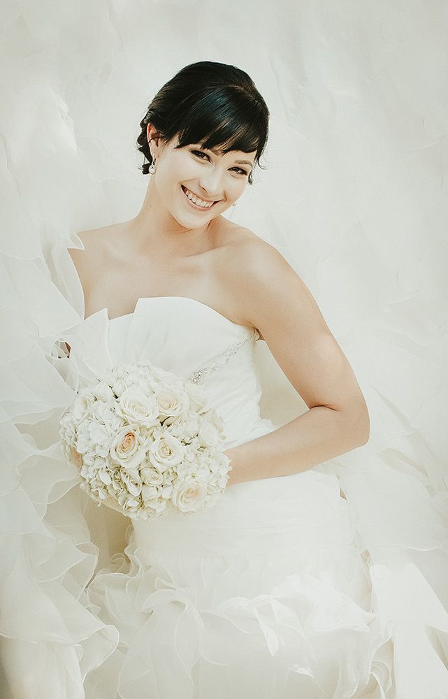 A delicate white wedding dress with floral details and ruffles captured in a soft, ethereal bridal photoshoot.