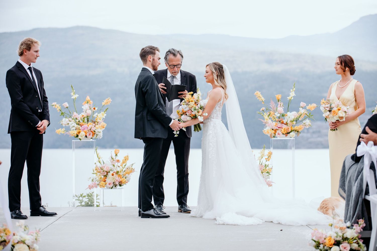 Wedding ceremony at 50th Parallel Winery with mountains and lake in background.