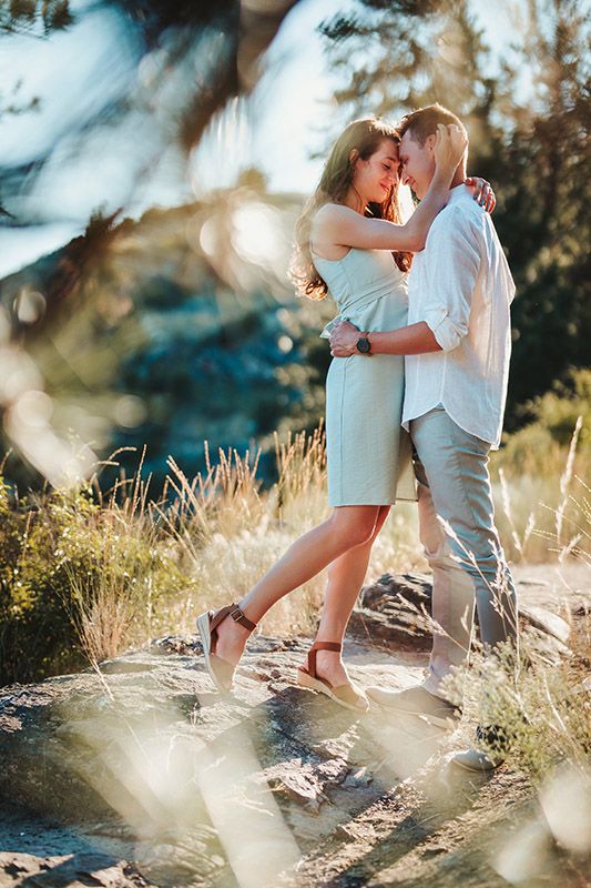 Romantic couple embracing on rocky terrain surrounded by golden sunlight and lush greenery outdoors.