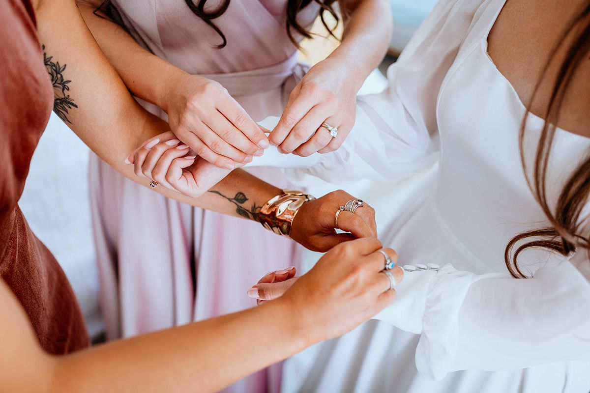 Hands fastening delicate jewelry clasps on a soft pink dress against white fabric.