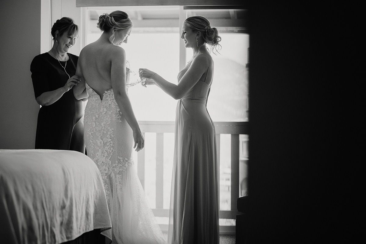 Silhouetted figures prepare for a wedding ceremony in black and white, with soft window light illuminating the scene.