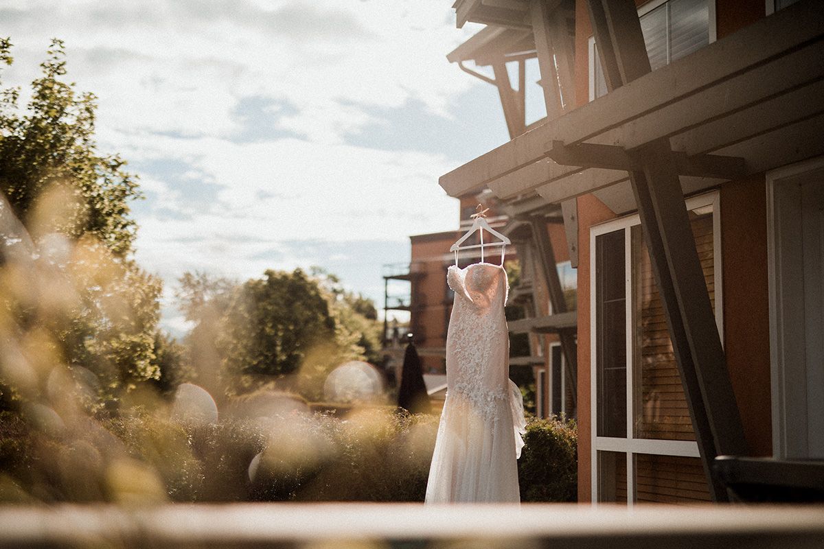 A wedding dress hangs elegantly against a rustic wooden door in warm sunset lighting.