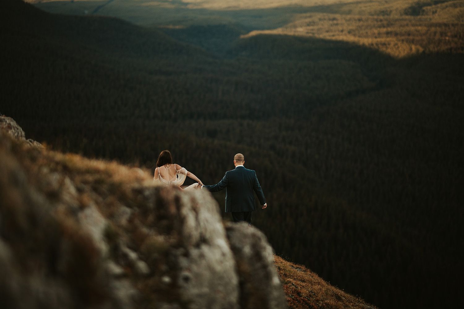 Scenic mountain landscape at sunset with two silhouettes sitting on a rocky cliff overlooking a dramatic valley.
