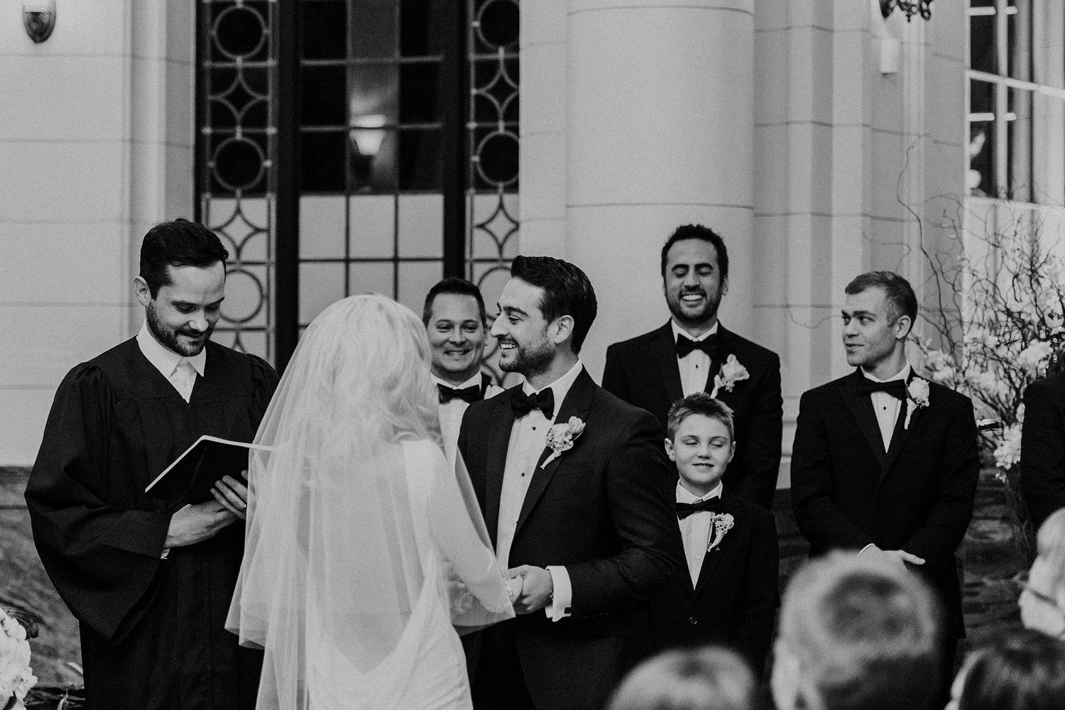 A black and white wedding photo showing a couple during their wedding ceremony in an elegant ballroom setting.