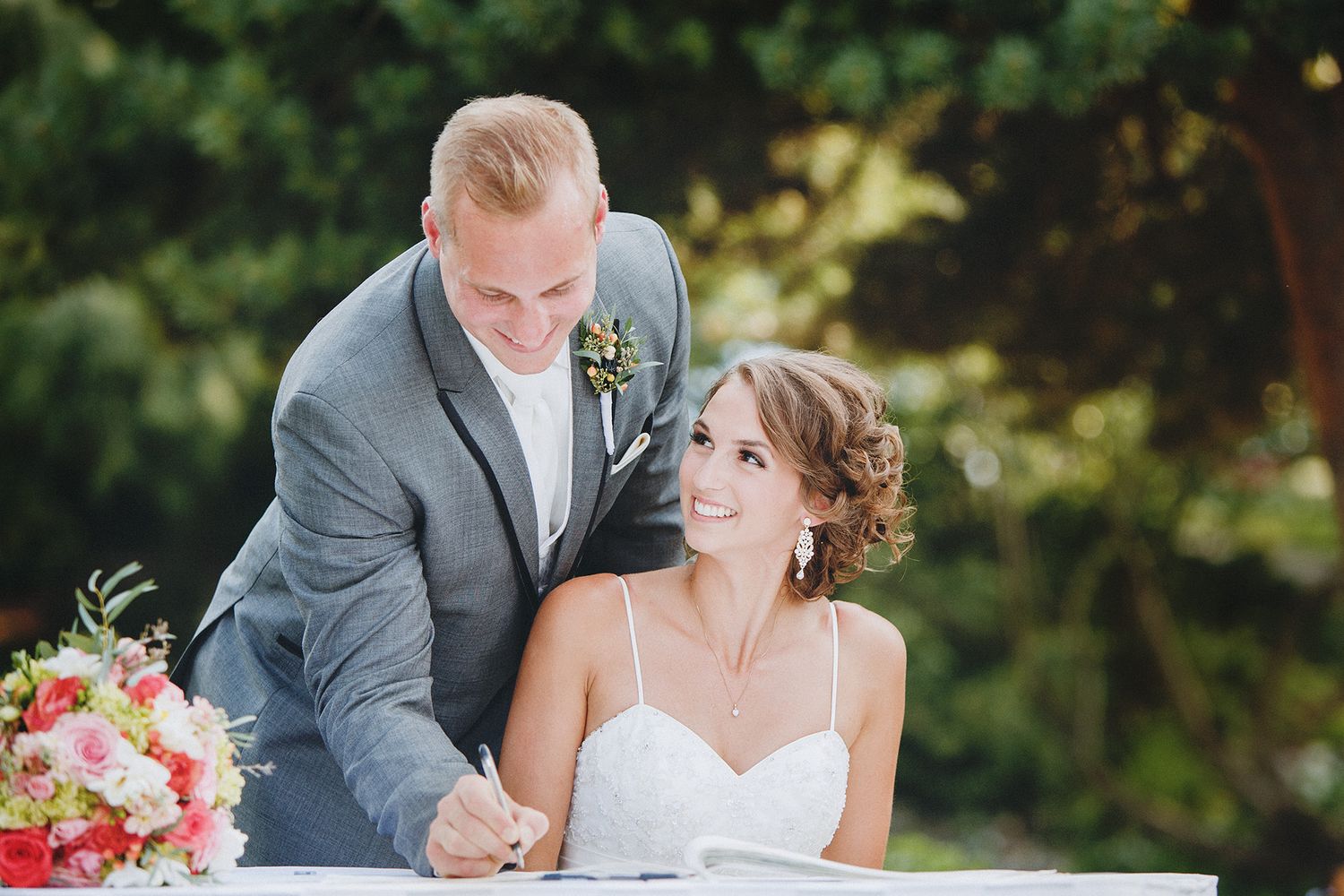 A romantic outdoor wedding ceremony with a couple embracing under lush green trees and natural lighting.