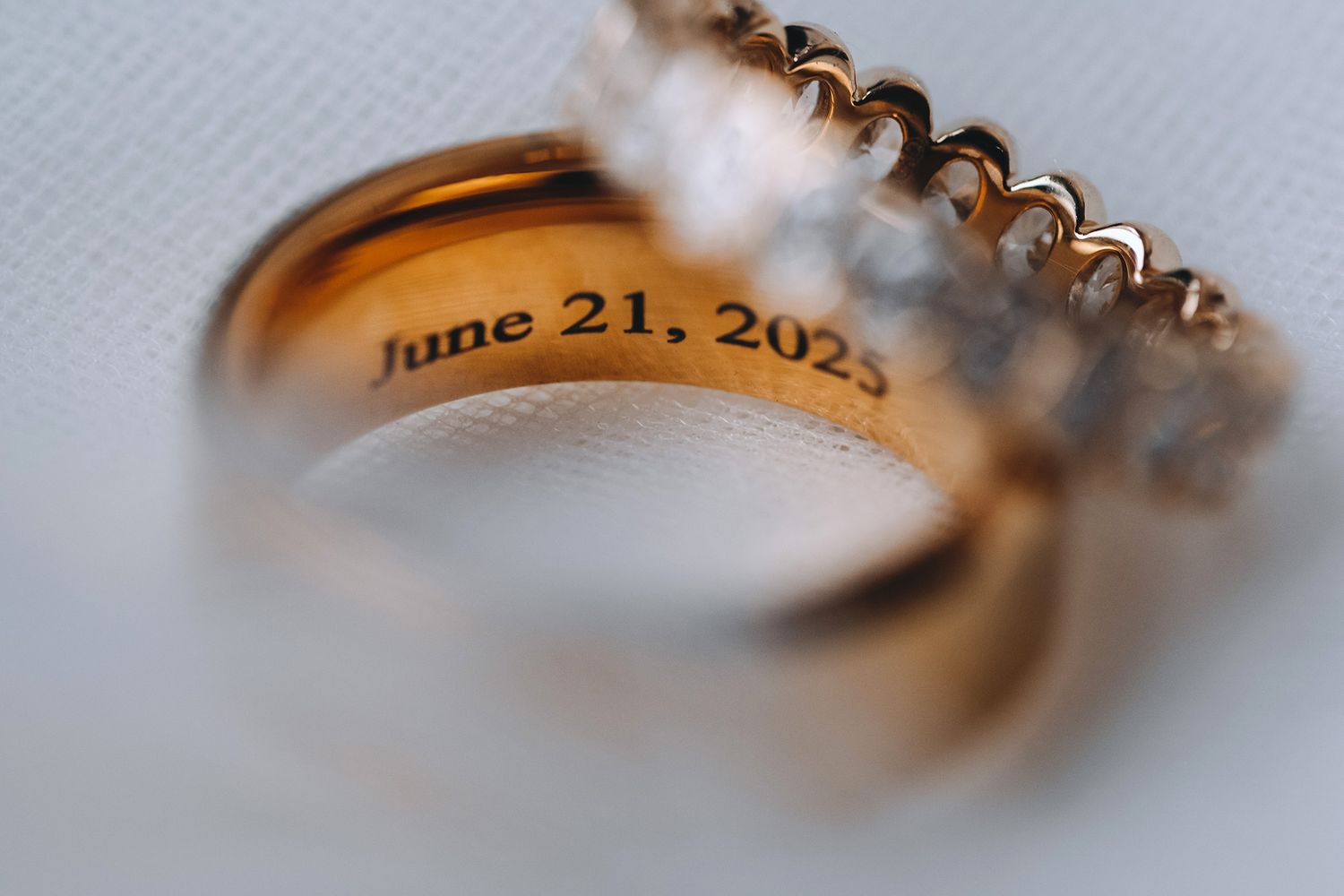 Close-up view of an engraved gold wedding ring with a date inscription reading June 21, 2025.