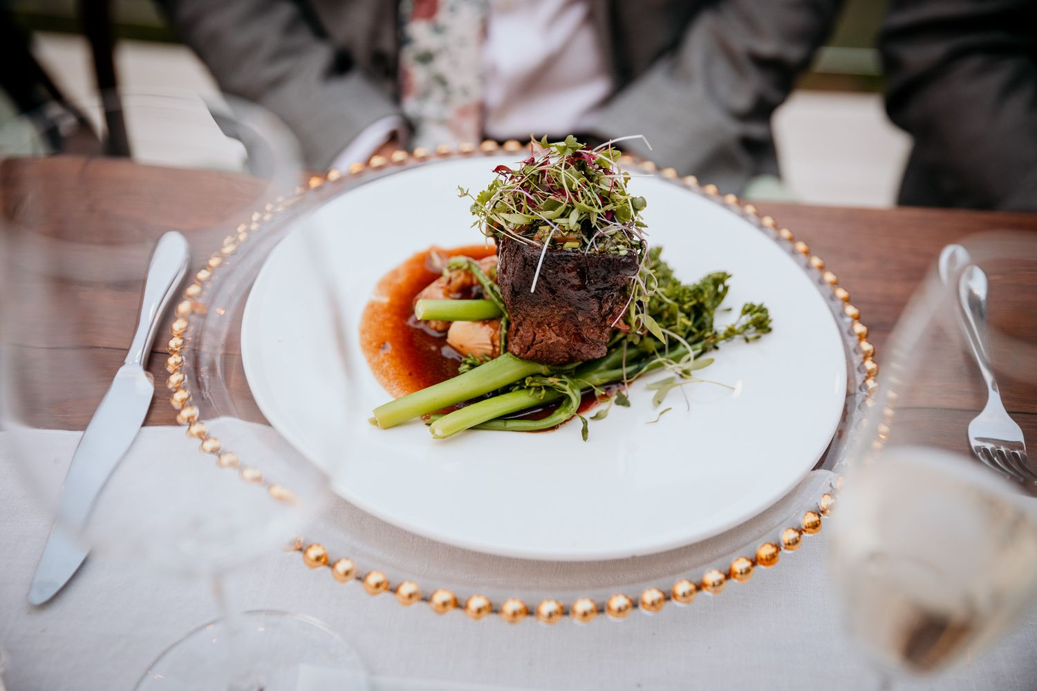 Elegant plated beef tenderloin with microgreens and asparagus served on a white plate with copper charger. during Vows and Vines wedding.