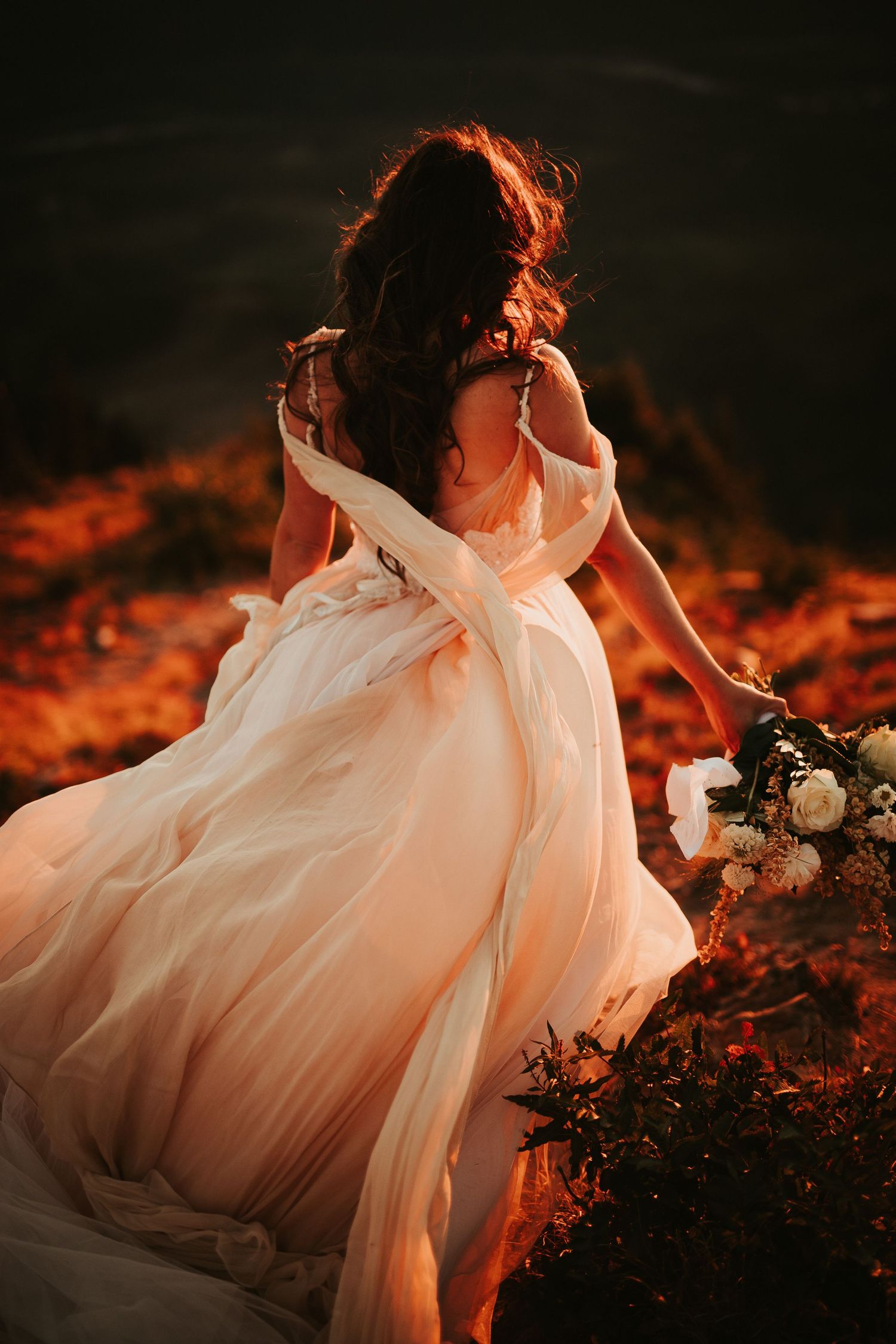 Ethereal pink wedding dress flowing in autumn sunlight with scattered leaves and delicate florals creating a dreamy scene.