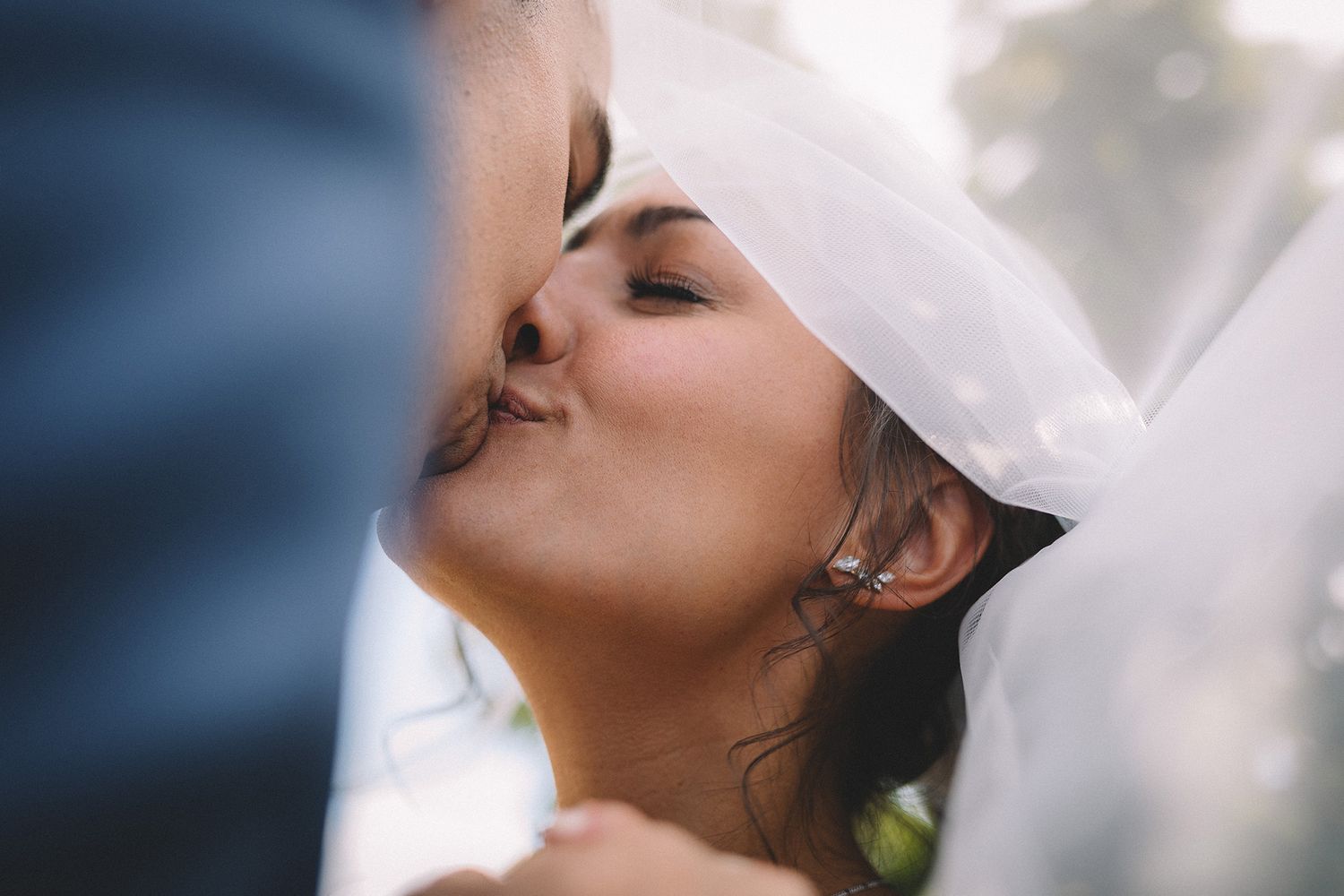 A bride looks upward with a serene expression while soft light filters through sheer white fabric in the background.