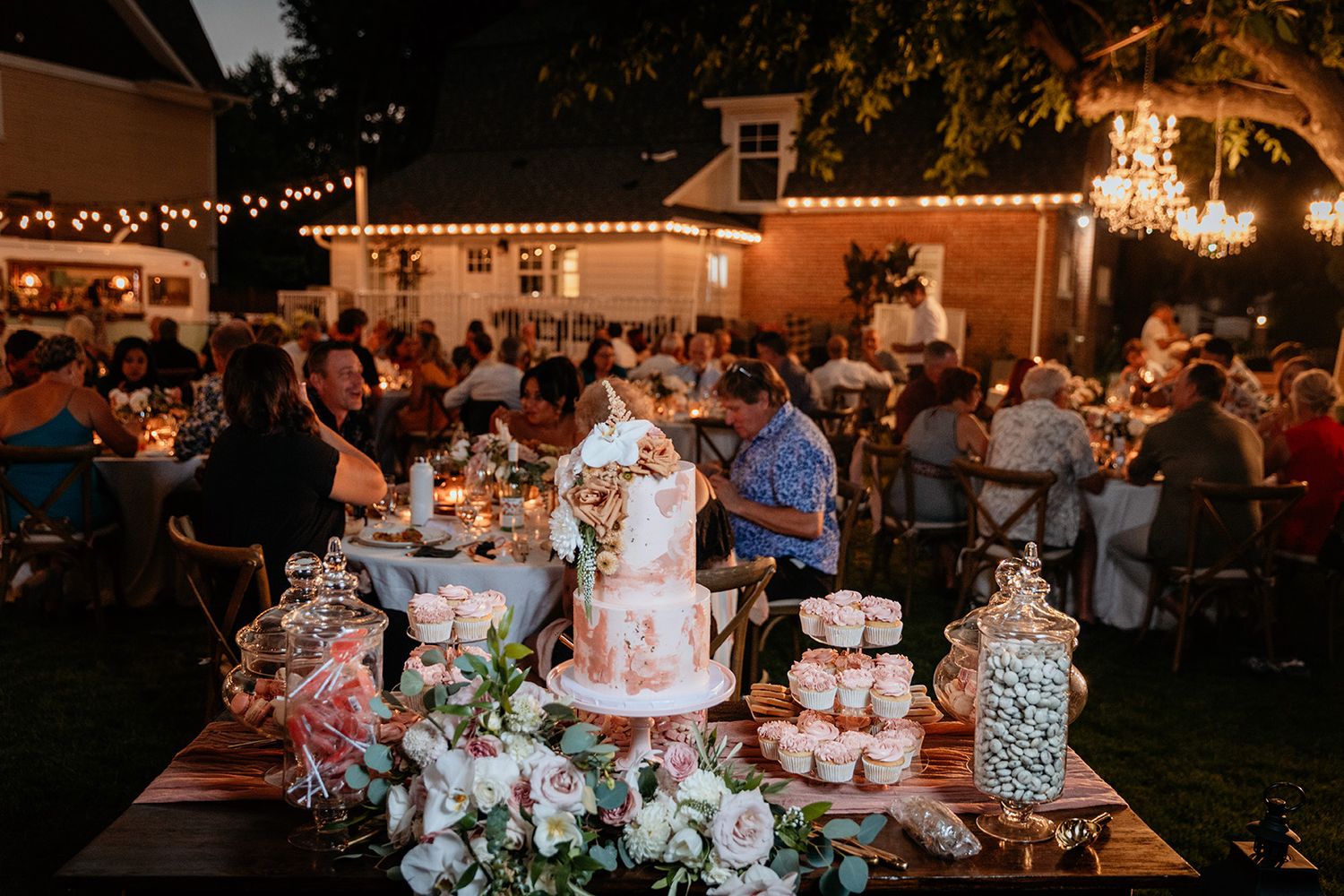 An outdoor wedding reception photo showing decorated tables, floral arrangements, and string lights at dusk.