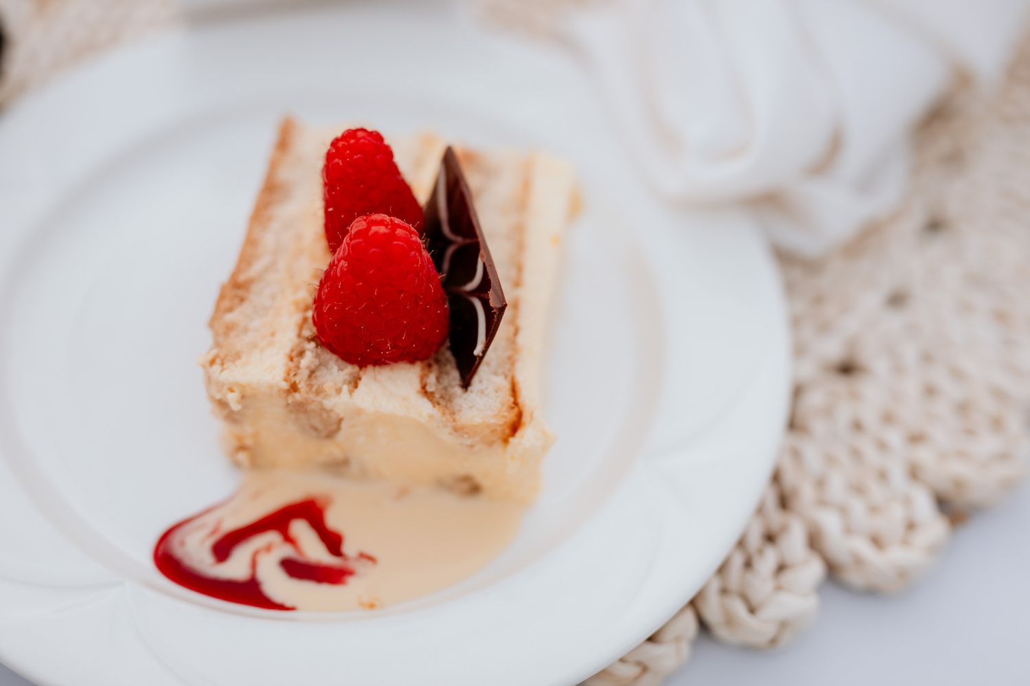 A close-up shot of a raspberry dessert with chocolate drizzle and whipped cream on a white plate.