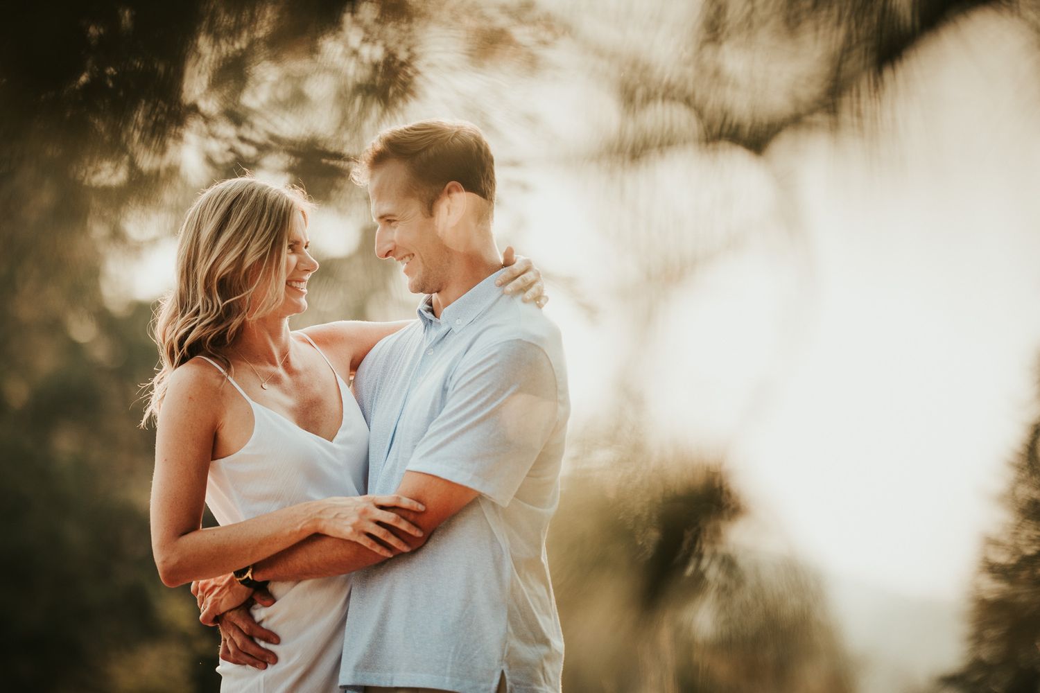 A couple embraces in warm sunlight with dreamy lens bokeh creating a romantic outdoor atmosphere.