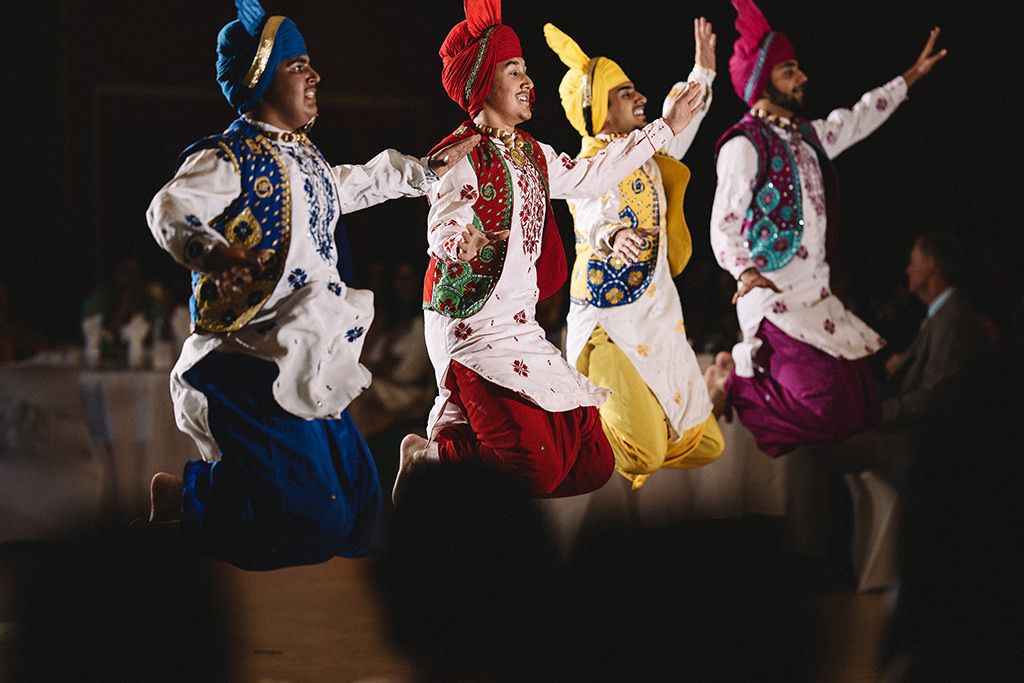 Colorfully dressed Bhangra dancers leap in synchronized motion wearing traditional Punjabi attire during a performance at a Kelowna wedding.