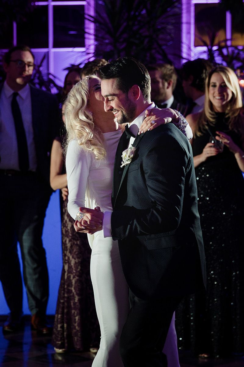 A couple shares a romantic first dance at their wedding reception under purple lighting.