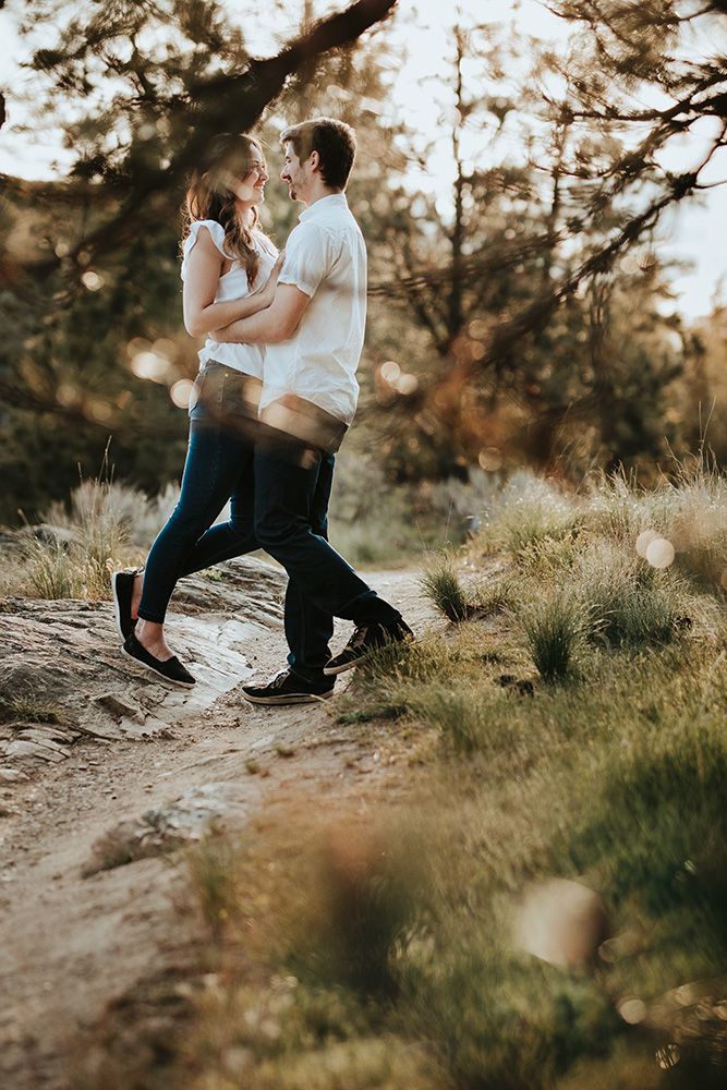 Couple embraces on a rocky hillside path during golden hour in a natural outdoor setting.