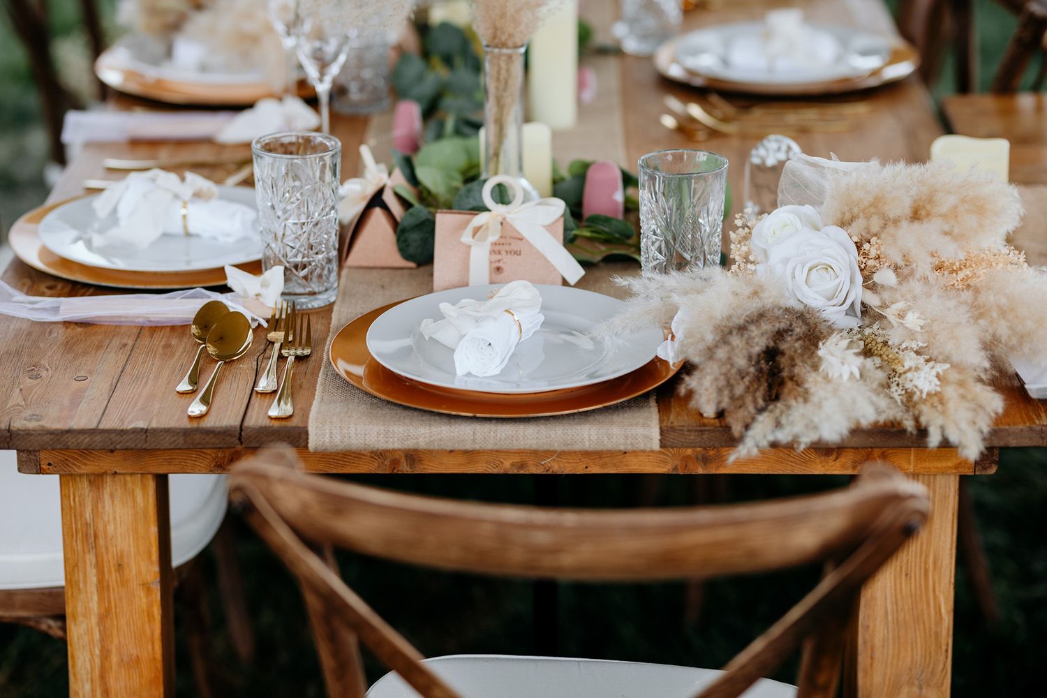 Rustic wooden table set with elegant place settings featuring pampas grass and crystal glassware for a boho wedding reception.