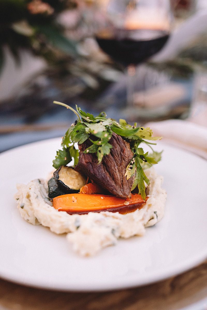Plated dish with seared meat, roasted carrots and fresh greens served on a white creamy sauce.