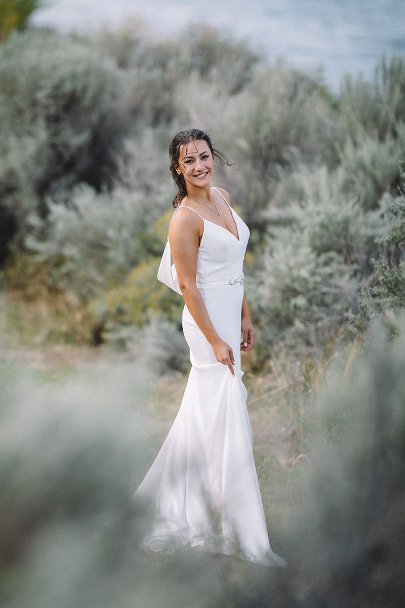 A bride in a flowing white dress poses gracefully against a backdrop of sage brush in a dreamy outdoor setting.