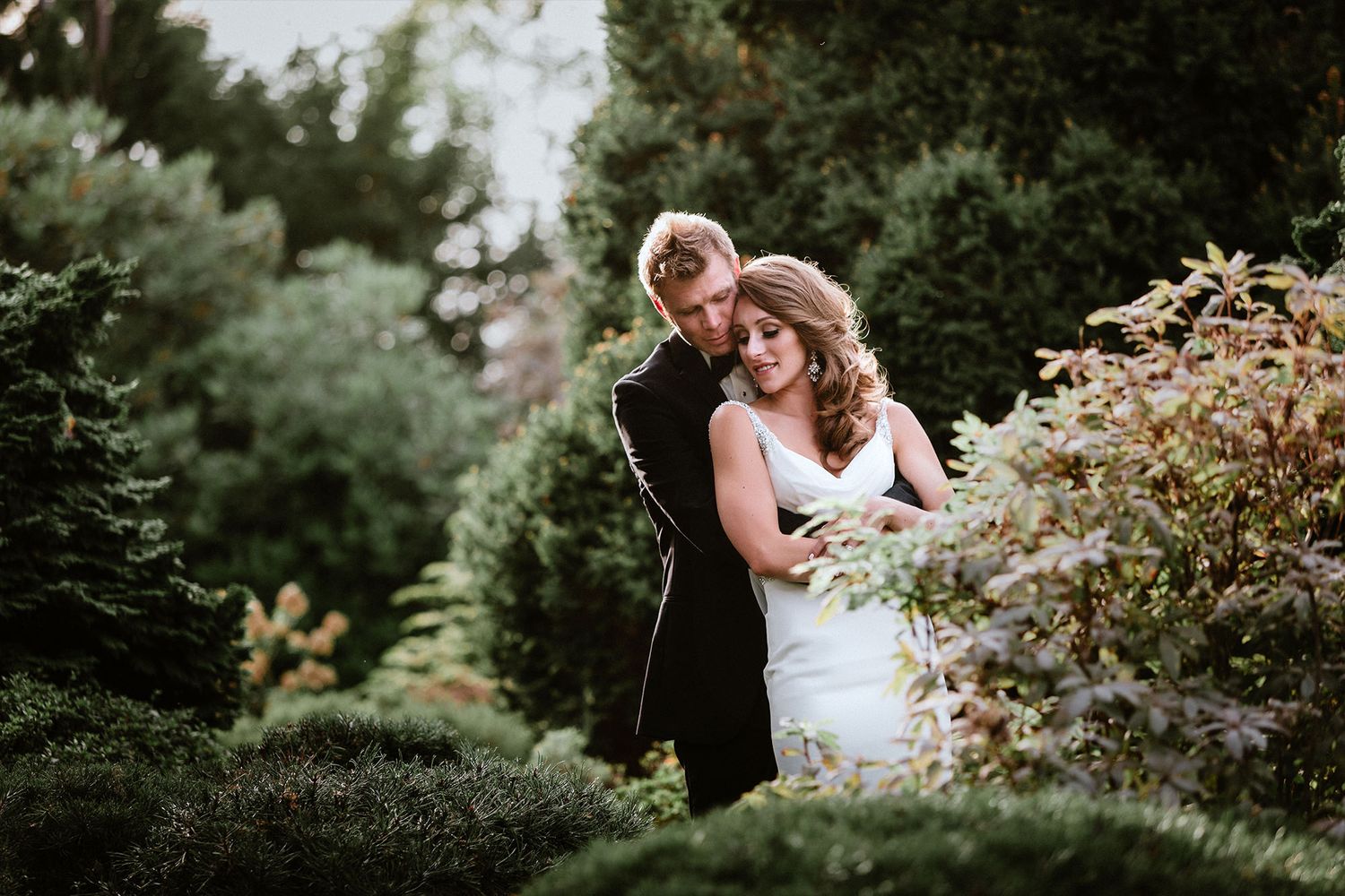 A couple embraces in a lush garden setting during a romantic outdoor photo session at Cecil Green Park House during sunset.