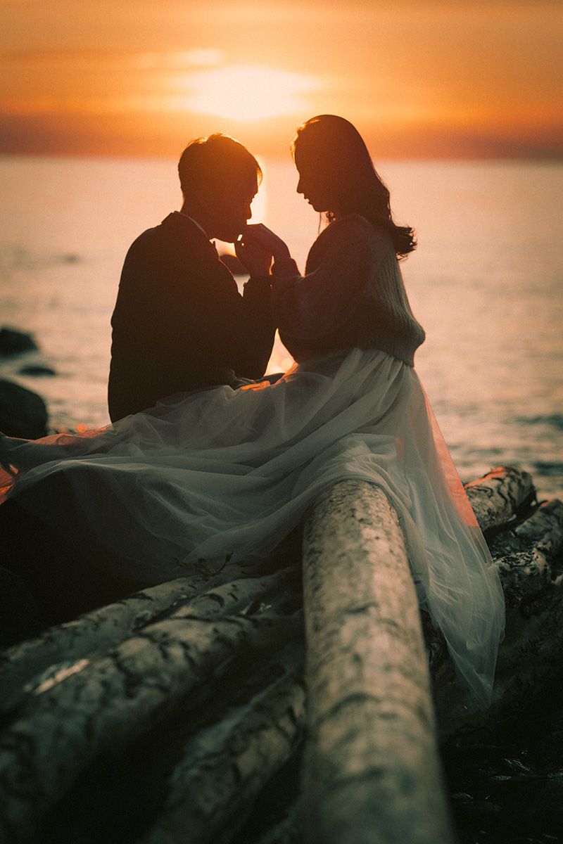 Romantic silhouettes of a couple sharing an intimate moment on a log by the ocean at golden sunset.