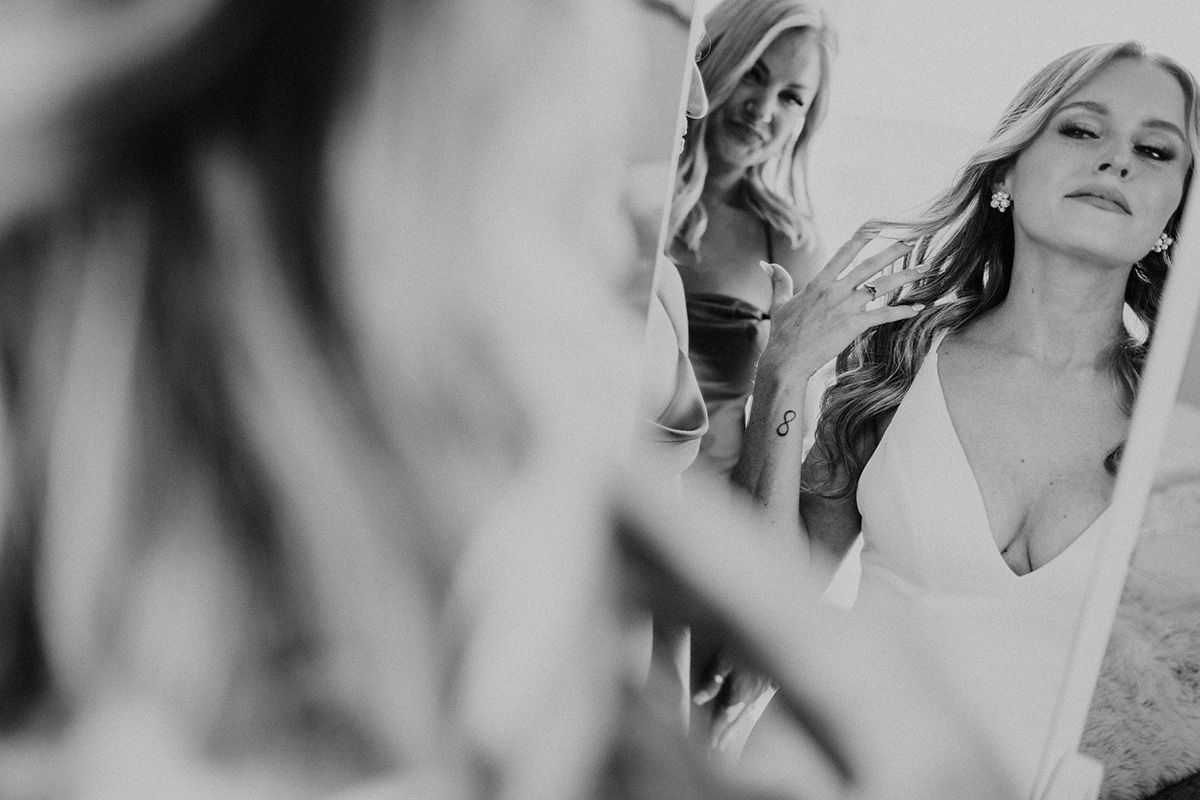 Black and white photo of a bride looking at her hair in a mirror.